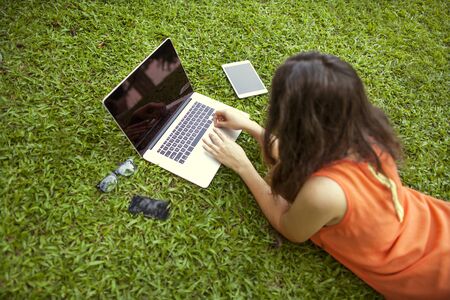 freelancer girl from the device: laptop, tablet, player, notebook, lying on the grass and working