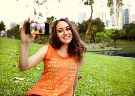 girl sitting in the park of Kuala Lumpur on the background of business centers and makes selfie, happyの写真素材