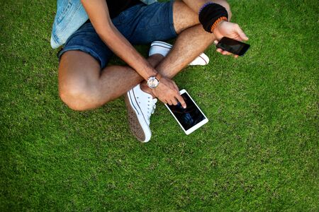 Outdoor portrait of modern young man with mobile phone, tablet on the grass.の写真素材