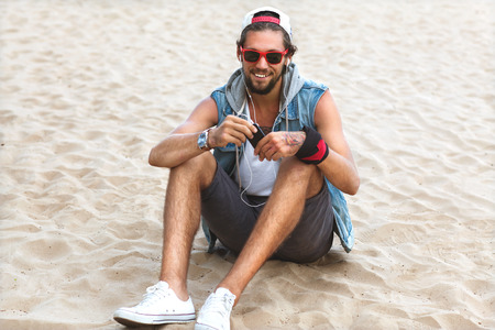 Hipster style boy. Fashion man sitting among the gray stone background is and listening to playerの写真素材