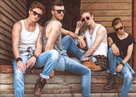 fashion hipster guys sitting near the wooden wall, dressed in jeans and a plaid shirt, sunglasses, Vogue Styleの写真素材