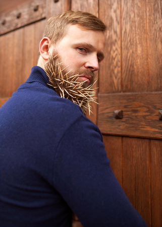 fashion hipster guy standing near a wooden door toothpicks in his beard, hatred, anger, contempt,...