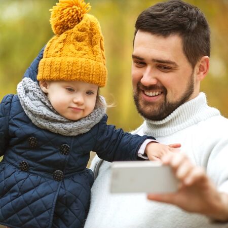 Family with a small daughter walk in autumn park with telephoneの写真素材