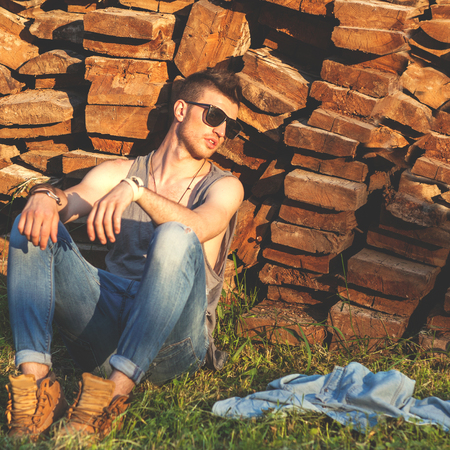 fashion man in denim clothes sitting near a wooden wall at sunsetの写真素材