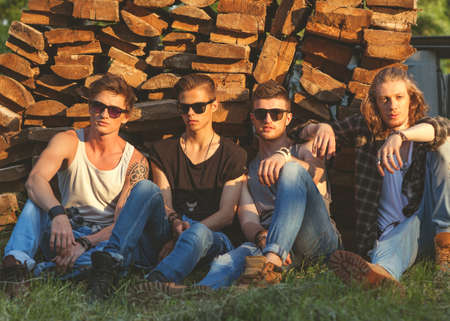 fashion guys friends sitting on the grass, wood backgrounds, sunsetの写真素材