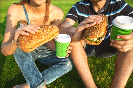 couple sitting on the grass in the park and eating sandwiches smilingの写真素材