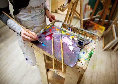 artist draws a picture in an apron, easel and paint paletteの写真素材