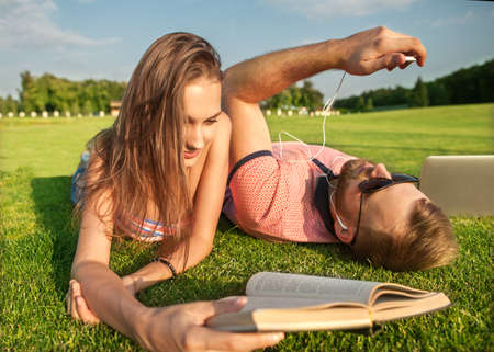 girl and guy lying on the grass reading a book relaxing in the parkÃ¢Â¨の写真素材