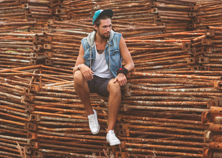 Hipster fashion man sitting on the iron frame begraund smiling