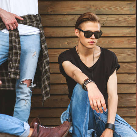 Fashion hipster guy sitting near the wall, dressed in jeans and a plaid shirt, sunglasses, Vogue Styleの写真素材