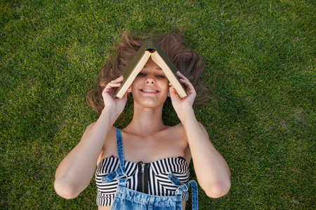 Girl lying on the green grass, listening to music on a white label trave- My Love and reading bookの写真素材