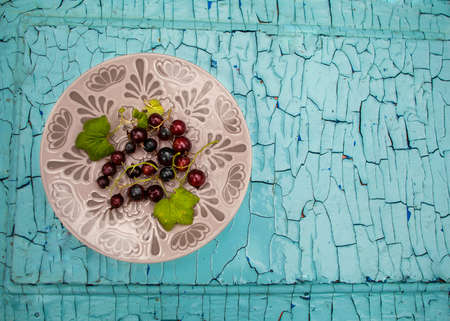 berries lie on a plate, a blue wooden background with cracked paint, healthy eating, currant berries with leavesの写真素材