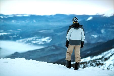 the guy is standing on top of a snowy mountain looking into the distance, the view from behindの写真素材