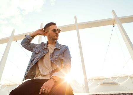 fashion guy sitting at sunset posing in sun glassesの写真素材