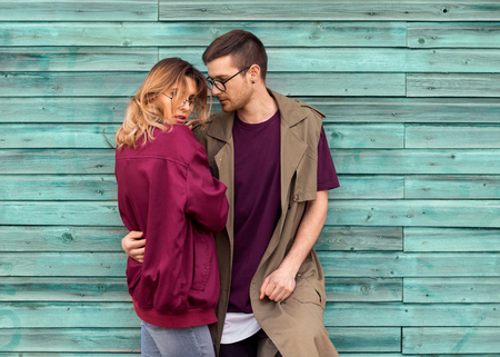 fashion couple in their glasses with burgundy clothes posing on a blue wooden wall