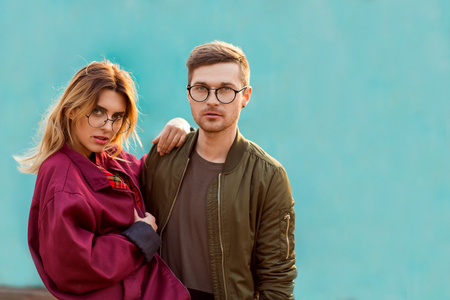 fashion couple in their glasses with burgundy clothes posing on a blue wooden wallの写真素材