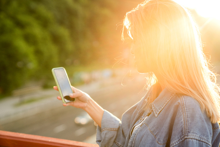 girl taking pictures of a landscape, close-up of a phone in her hand at sunsetの写真素材