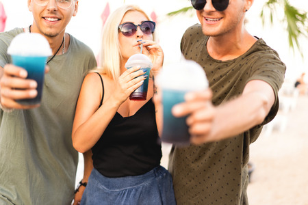three friends cheerful company rest on a tropical beach and drink cocktails, very, magazine conceptの写真素材