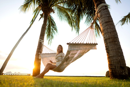 girl in a hammock tropical palm trees enjoying a  vacation at sunsetの写真素材