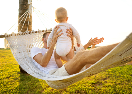 happy family on a tropical island at sunset lie in a hammock and play with their sonの写真素材