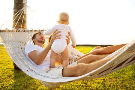 happy family on a tropical island at sunset lie in a hammock and play with their sonの写真素材