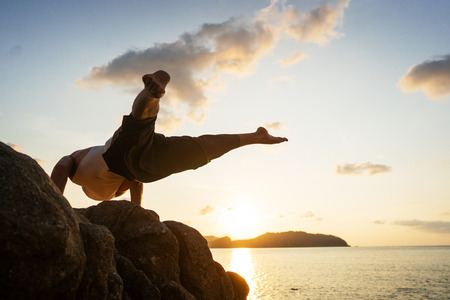 guy doing acrobatic yoga at sunset by the seaの写真素材