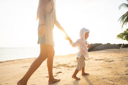 mother playing with her son at sunset on a tropical beachの写真素材
