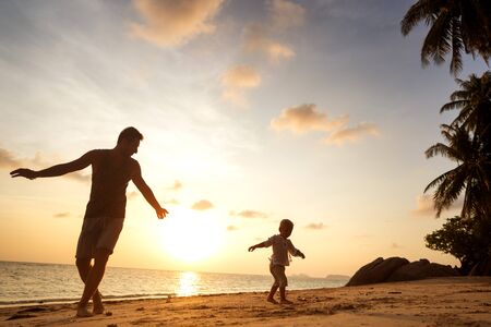 dad and son playing on the sand at the beach at sunsetの写真素材