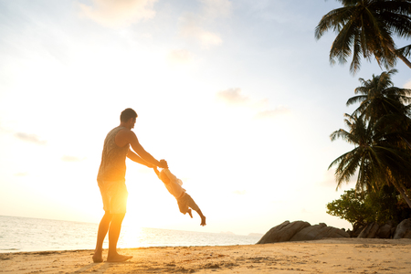 dad and son playing on the sand at the beach at sunsetの写真素材
