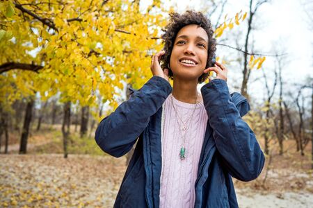 beautiful african girl in autumn park listening to music outdoors smilingの写真素材