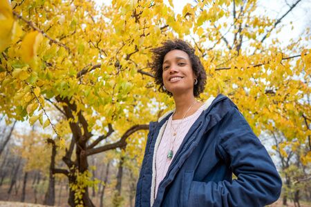 beautiful african girl in autumn park listening to music outdoors smilingの写真素材