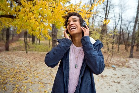 beautiful african girl in autumn park listening to music outdoors smilingの写真素材