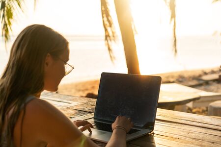 freelancer girl with a computer among tropical palm trees work on the island in sunsetの写真素材
