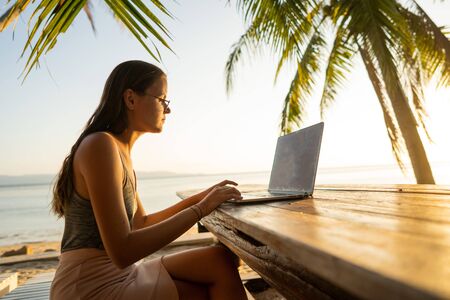 freelancer girl with a computer among tropical palm trees work on the island in sunsetの写真素材