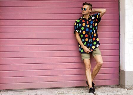 fashion guy in sunglasses posing on a pink wallの写真素材
