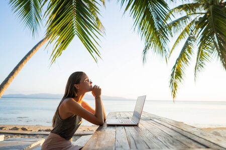 freelancer girl with a computer among tropical palm trees work on the island in sunsetの写真素材