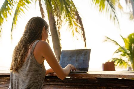 freelancer girl with a computer among tropical palm trees work on the island in sunsetの写真素材