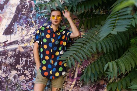 fashion guy in sunglasses posing on a painted wall in palm leavesの写真素材