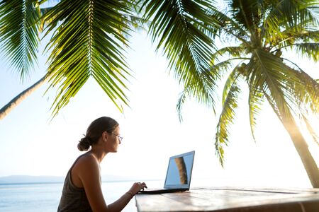 freelancer girl with a computer among tropical palm trees work on the island in sunsetの写真素材