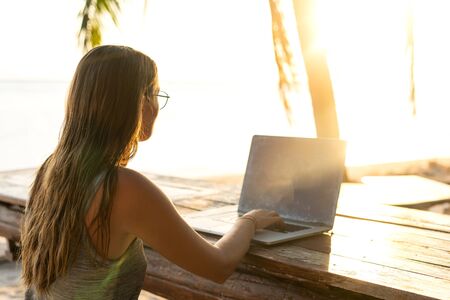 freelancer girl with a computer among tropical palm trees work on the island in sunsetの写真素材