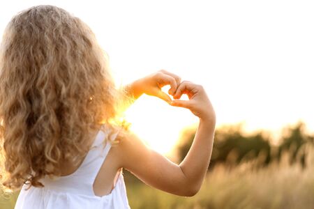 little girl at sunset shows a heart with hands plays in the fieldの写真素材