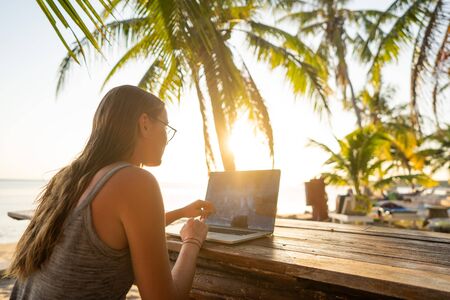 freelancer girl with a computer among tropical palm trees work on the island in sunsetの写真素材