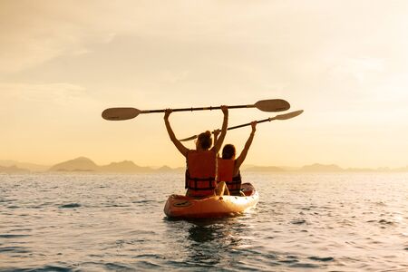 Couple kayaking together. Beautiful young couple kayaking on lake together and smiling at sunsetの写真素材