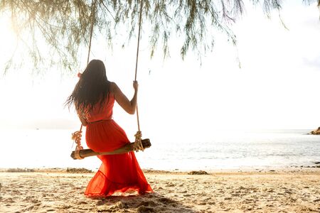 girl in a red dress on a swing among tropical palm trees in Thailand at sunsetの写真素材