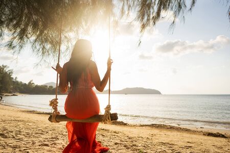 girl in a red dress on a swing among tropical palm trees in Thailand at sunsetの写真素材