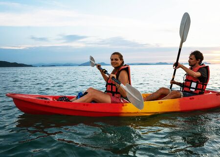 Couple kayaking together. Beautiful young couple kayaking on lake together and smiling at sunsetの写真素材