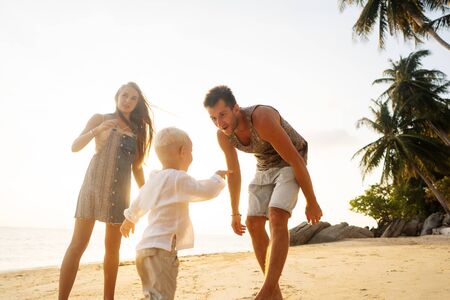 family happily walk along a tropical beach at sunsetの写真素材