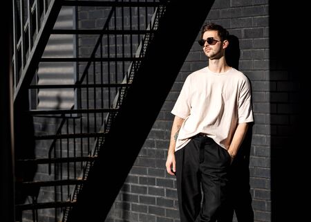fashion guy stands posing near a black brick wall in sunglassesの写真素材