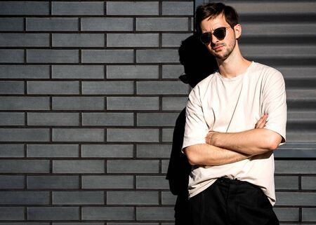 fashion guy stands posing near a black brick wall in sunglassesの写真素材