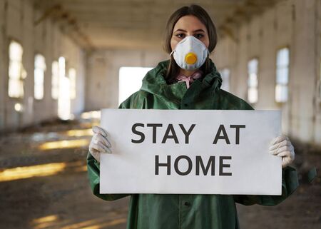 Doctor wearing protection face mask against coronavirus. Staff preventive gear. Holding a poster stay at home in handsの写真素材